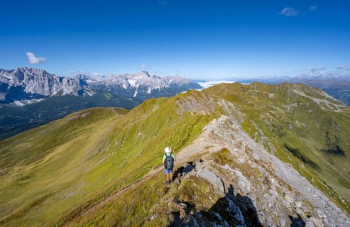 Mountaineers on a hiking trail between green mountain meadows on a mountain ridge, mountain
