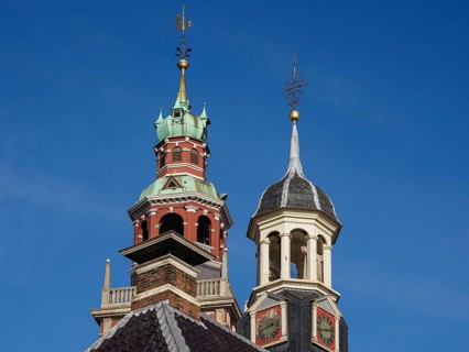Two historic church towers with weather vane and clock under a blue sky, two towers of historic