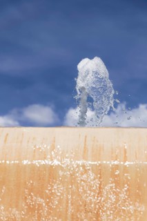 Stream of water coming out of a public fountain with a blue sky in the background