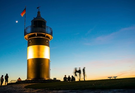 Black and white lighthouse, called 'Kleiner Preusse', stands illuminated at night shortly after