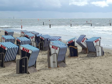 Several blue and white beach chairs stand on a sandy beach with a cloudy sky and the sea in the
