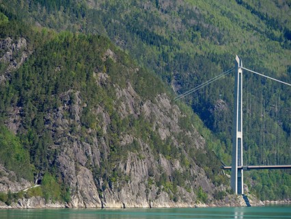 High bridge over turquoise water, surrounded by forested mountains and rocky cliffs, bridge in a