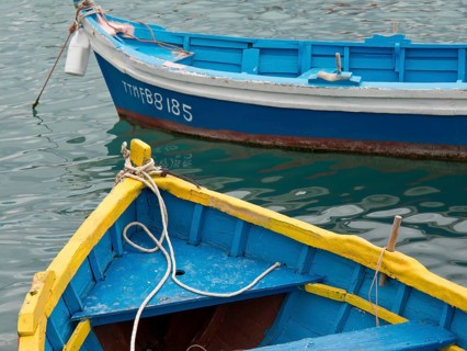 Two small boats in different colours floating in the harbour water, connected with ropes, many