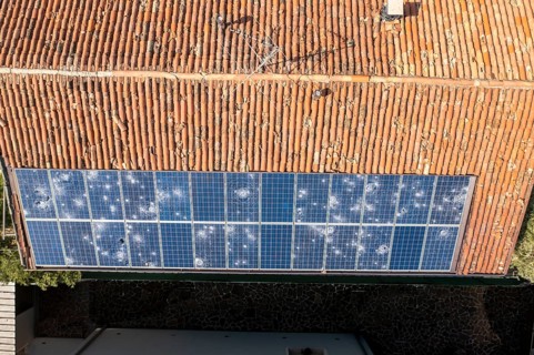 Aerial image of a terracotta tiled roof with a row of damaged solar panels