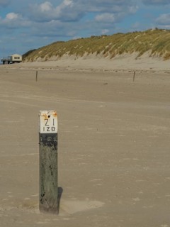 Close-up of a numbered post in a sandy coastal area under a cloudy sky, clouds on the beach with