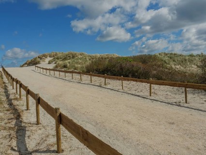 A sandy path lined with a wooden fence, sandy dunes and a sky with clouds, dunes on an island with
