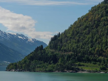 Tranquil landscape with a lake, green mountains and snow-capped peaks under a blue sky, greenish