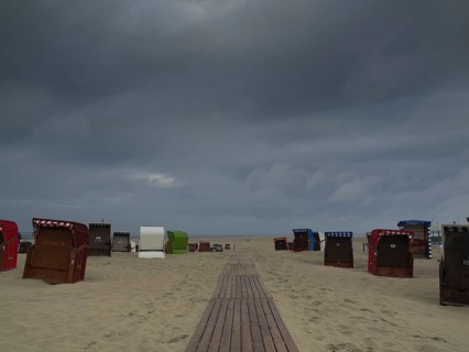 Dark clouds hanging over a beach with scattered beach chairs and a wooden jetty, beach chairs and