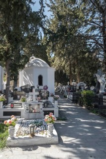A white chapel surrounded by tombstones and an angel statue in a peaceful cemetery, Lindos, Rhodes,