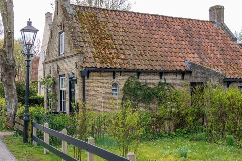 Rustic brick house with tiled roof and garden in spring, green vegetation and cosy atmosphere,