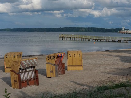 Several beach chairs on the beach, a long pier, cloudy sky and calm sea in the background, beach