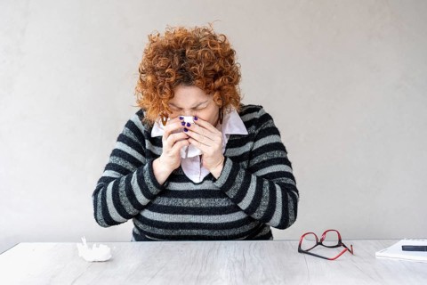 A woman with a red head and black and gray striped sweater is blowing her nose