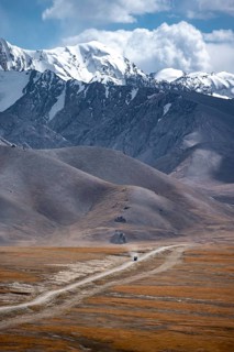 Car on a gravel track in the high mountain plateau, glaciated and snow-covered peaks, Ak Shyrak