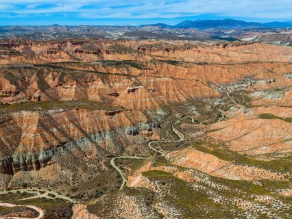 Extensive desert landscape with red rocks and canyons, criss-crossed by serpentines, aerial view,