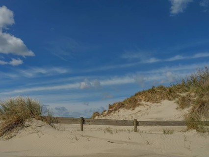 Sand dunes on the beach under a clear blue sky with scattered clouds and tufts of grass, beach and