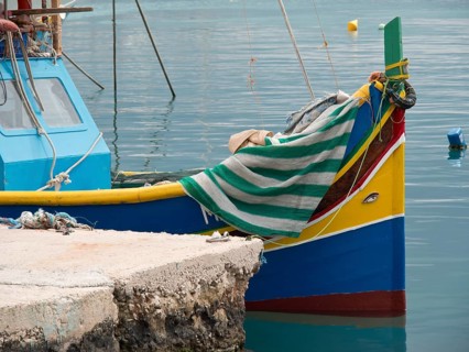 Small colourful boat moored at the pier, covered with a striped cloth, many colourful fishing boats