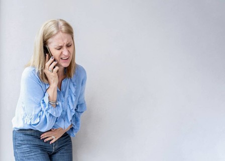 A blonde woman is calling her doctor because she is suffering an appendix pain