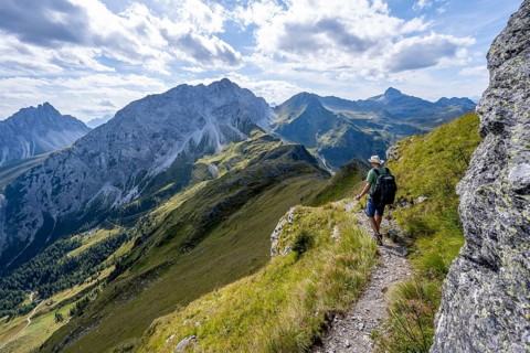 Mountaineer on a hiking trail on a grassy mountain ridge, idyllic mountain landscape with green