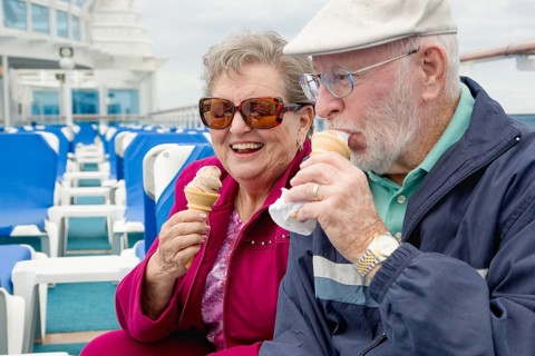 Happy senior adult couple enjoying ice cream on the deck of a luxury passenger cruise ship