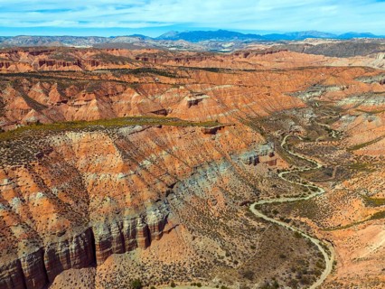 Red rocks and canyons criss-crossed by serpentine roads, embedded in a vast desert landscape,