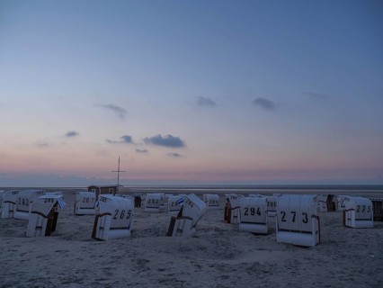 A calm dusk on a beach with white beach chairs and a soft sky, setting sun on a beach with beach