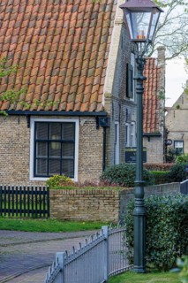 Quiet rural scene with a brick house and a street lamp surrounded by green foliage and a garden
