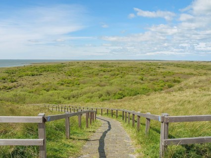A wooden path leads through the dunes, the sky is blue and covered with clouds, in the background