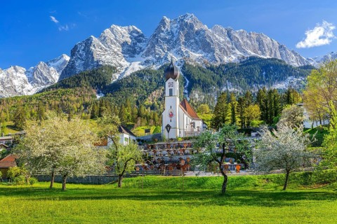Spring meadow with blossoming trees and parish church in front of the Grosser Waxenstein 2277m in