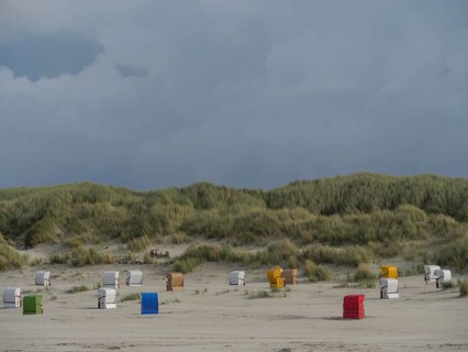 Beach chairs are spread out in front of a hilly dune landscape under a cloudy sky, colourful beach