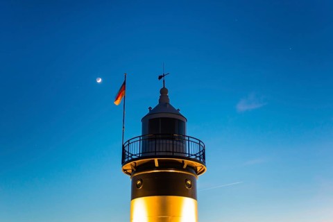Black and white lighthouse, called 'Kleiner Preusse', stands illuminated at night shortly after
