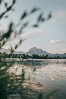 Quiet lake with a jetty, surrounded by mountains and trees. Hopfensee, Bavaria Germany