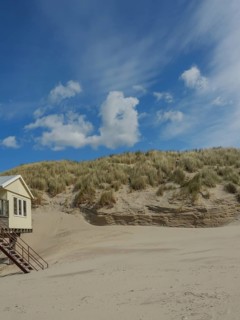 Small house on the edge of a sand dune under a clear sky with few clouds, clouds on the beach with