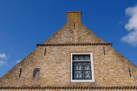 Close-up of a rustic brick house gable with a window under a bright blue sky, historic houses and a