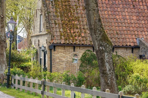 Historic house with brick wall, fence and street lamp, surrounded by trees and a garden, historic
