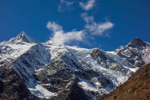 Snowy mountains and glaciers under a blue sky with some clouds, snow on high mountains in the alps,