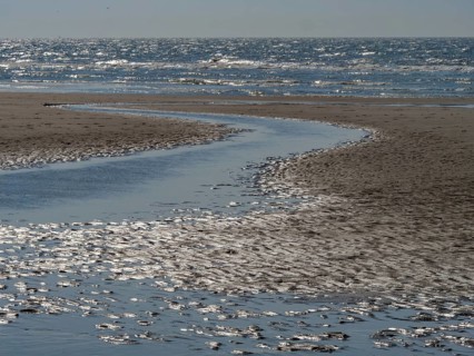 Beach with a gently curving watercourse in the sand and blue sea in the background, glittering sea