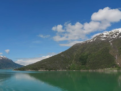 Clear water, snow-capped mountains and blue sky in a peaceful landscape, greenish shimmering water