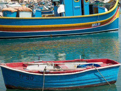 A small red boat and a larger fishing boat moored in the harbour, many colourful fishing boats in a