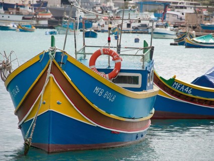 Front view of a colourful boat and another boat next to it in a quiet harbour, life ring visible,