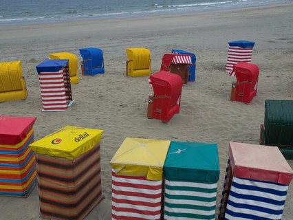 Colourful beach chairs spread out on the beach in different colours under a cloudy sky, beach