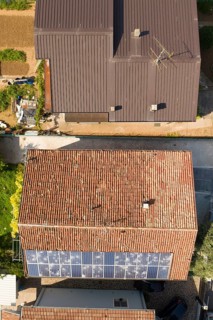 Aerial shot of a residential area showing roofs with damaged solar panels and brown tiles