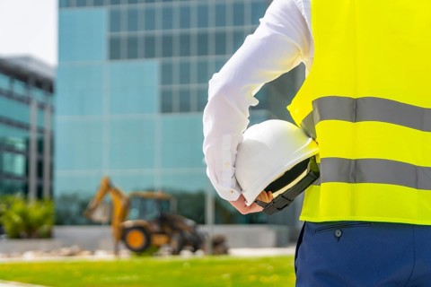 Rear view of an unrecognizable architect holding a helmet observing remodeling works in a financial