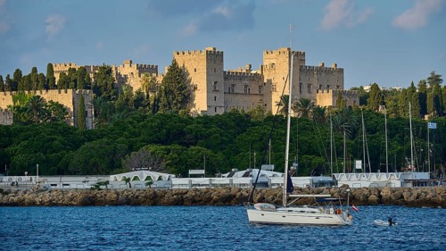 Historic castle by the sea with yacht in the foreground and cloudy sky, trees, Grand Master's