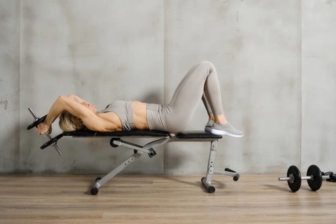 A muscular woman lies on a bench in the gym and pushes a dumbbell behind her head with both hands