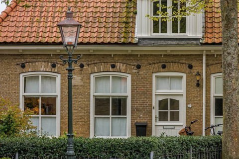 An old brick house with white windows and a lamppost in the foreground, old houses with green