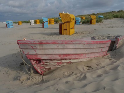 Red boat in the sand with scattered beach chairs and dunes, peaceful atmosphere, colourful beach