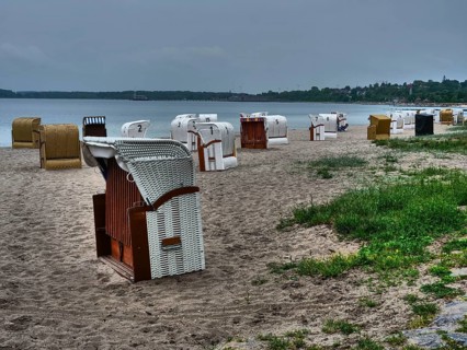 Beach chairs on a sandy beach with the sea in the background under a cloudy sky. Green plants are