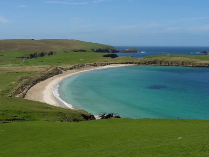 A tranquil coastal landscape with grassy hills, a gently curving beach and emerald green waters