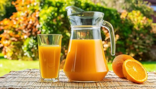 A glass of orange juice and a carafe on an outdoor mat with a green background, AI generated, AI