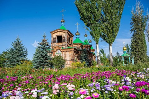 Colourful flowers in front of the Russian Orthodox Church Cathedral of the Holy Trinity, wooden